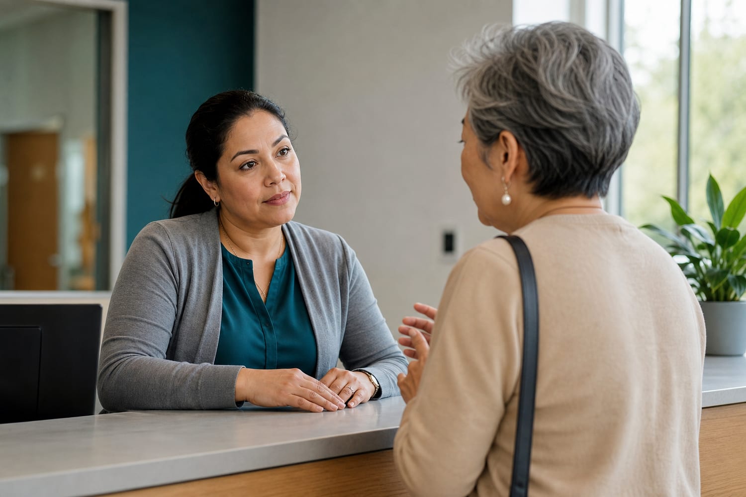 A warm and capable patient-access coordinator assisting a visitor at a modern healthcare front desk